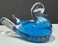 Blue glass bird paperweight viewed from the left side showing clear head and tail with blue body containing bubbles.