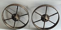 Pair of antique cast iron wheels laid flat side by side showing full face of wheels with central hub and spokes.