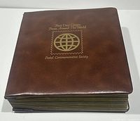 Closed brown binder with gold text and a globe logo titled 'First Day Covers From Around The World Postal Commemorative Society'