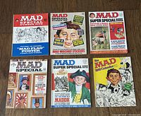 Photo of the 6 vintage MAD magazines laid out on a wooden surface showing all covers clearly.