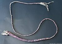 Dark brown hand-woven rawhide whip laid out on a black background, showing full length and braided texture.