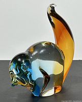 Side view of multicoloured Murano style glass lemur paperweight showing amber and blue hues and curved tail