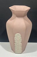 Front view of hexagonal pink pottery vase with white raised leaf design on black background