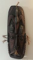 Front view of carved tribal wooden mask with bird figure, faces and intricate carvings