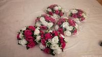 Six artificial flower ball arrangements with pink and white roses placed on a table.