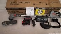 Lot items arranged on a flat surface showing all components of the battery weed wacker kit including main unit, batteries, charger, blade, toolkit and manual.