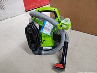 Photo of a lime green and black Bissell Little Green ProHeat portable carpet cleaner with a grey hose and red brush nozzle attachment, coiled cord, and instruction label visible on device.
