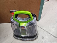 Front and top view of the Bissell Little Green ProHeat showing handle, clear water tanks, and attached hose.