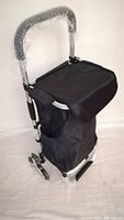 Foldable shopping trolley standing upright with black removable bag and metal frame, handle covered in protective bubble wrap.