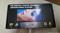 Top view of HD digital photo frame advertising player box with image of woman with colorful face art on screen and icons of supported functions