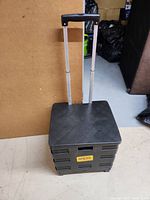 Photo showing the rolling storage cart with the telescopic handle extended, flat top surface, and black plastic construction.