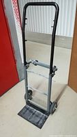 Front view of metal hand truck dolly cart with black handle, tubular metal frame, and base plate.