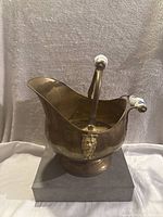 Front view of antique brass bucket showing curved shape and porcelain handle with blue floral pattern