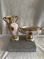 Porcelain bowl and vase side by side on a grey surface with a white textured backdrop, showing their decorative patterns and shapes.