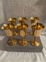 Front view of six brass golden goblets arranged in two rows of three, showing the twisted stems and flared golden cups.