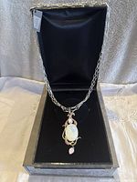 Front view of elegant silver-tone necklace with large oval faceted MM Crystal Swarovski pendant accented with pink stones in black display box.