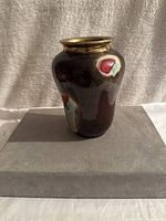 Front view of a glossy brown ceramic vase with red, turquoise, and cream spots and a gold rim, standing on a grey base.