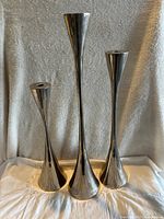 Three metal candle holders grouped on fabric backdrop showing full height and varying sizes