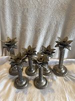 Front view of six metal candle holders with leaf pattern design, arranged in two rows, against fabric backdrop.