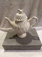 Front angle of the white porcelain pot showing geometric diamond texture and bird on lid.