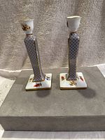 Front view of both candle holders showing tapered column design with blue geometric pattern, gold trim, and floral base.