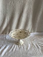 Porcelain cake stand showing top view with scalloped and lattice edges, decorated with small colorful flowers and bees.