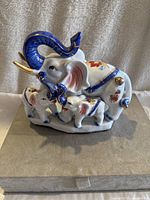 Front view of porcelain elephant family figurine with floral and blue accents, placed on a fabric base.