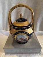 Front view of the porcelain urn showing gold and navy blue detailing and painted scene