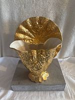 Front view showing scalloped edge and ornate gold textured floral design on the body and gold fan-shaped backplate with embossed detail.