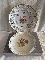 Two Schumann Bavarian porcelain plates featuring pierced lattice rims and floral motifs, one round scalloped with gold trim and one octagonal with central floral design.