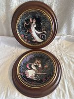 Pair of round porcelain decorative plates mounted in wooden frames with Thai artwork and floral motifs.
