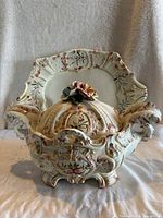 Front view of the ornate vintage Bassano tureen with lid showing the floral sculpted top and intricate raised patterns, platter visible behind