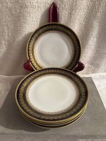 Four porcelain plates stacked, showing one plate on a stand with detailed cobalt blue and gold borders.
