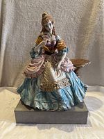 Front view of a porcelain figurine of a Victorian lady holding a fan, in a multicolored dress.