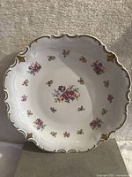 Front view of the white porcelain plate showing scalloped gold-trimmed edges and floral decorations at center and rim.