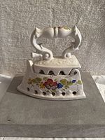 Front and side views of the white ceramic decorative iron figurine with floral design and ornate handle, showing crazing on glaze and colorful hand-painted flowers.