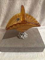 Side angle showing amber crystal vase with handle and scalloped edge on metal flower stand