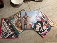 Several vinyl record album covers on floor showing Rocky Horror Picture Show, Star Wars, Grease and more from 80s movies and music