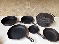 Top-down photo showing full set of six cast iron pieces including Dutch oven and frying pans on a white surface.
