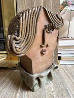 Front angle view showing stylized hair, eye with eyelashes, nose, lips, and base resembling folded fabric