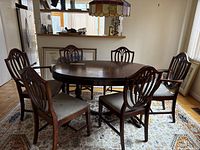 Full set of six wooden dining chairs around a wooden dining table on a decorative rug.