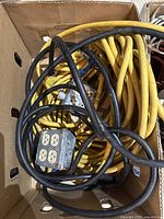 Box containing yellow and black extension cords with a metal four-outlet connector visible