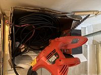 Close-up photo of Black and Decker electric hedge trimmer with long black cord and some manual guides.