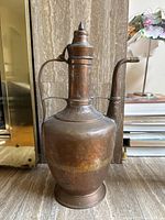 Front view of large copper coffee or tea pot showing dramatic narrow neck, pointed lid, curved spout and loop handle with visible patina and oxidation.