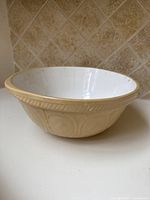 Side angle showing beige exterior with embossed circular pattern and wide rim.