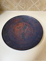 Top front view of the round ceramic plate showing abstract artistic faces in dark and rust colors.