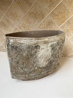 Oblong ceramic vase with textured and abstract surface seen from front angle showing shape and glaze pattern.