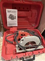 Milwaukee circular saw inside a red carrying case with power cord and operator manual.