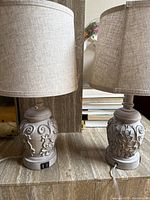 Pair of beige linen-shaded table lamps with ornate carved bases and USB ports visible on bases.