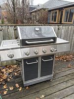 Full front view of large propane grill with multiple control knobs, side burner, and storage cabinet beneath.